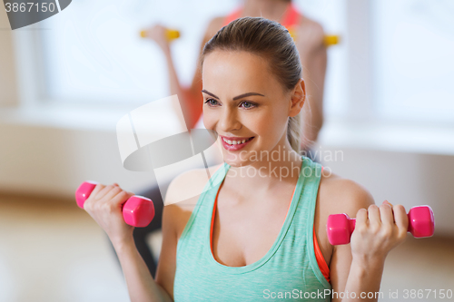 Image of smiling woman with dumbbells exercising in gym