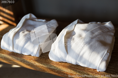 Image of close up of two white bathrobes on wooden shelf