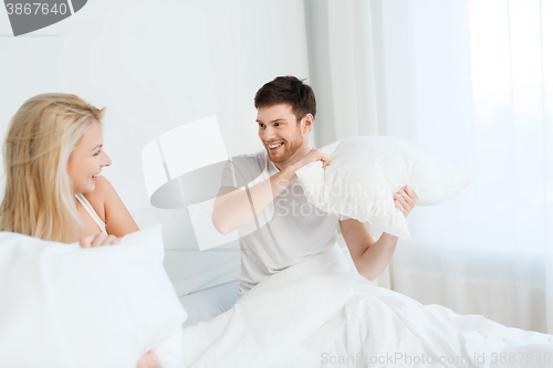 Image of happy couple having pillow fight in bed at home