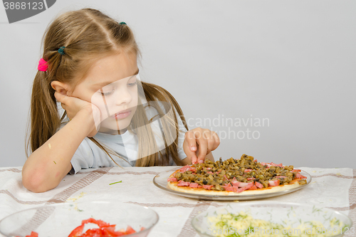 Image of Little six year old girl sitting at the table and picks unfinished pizza