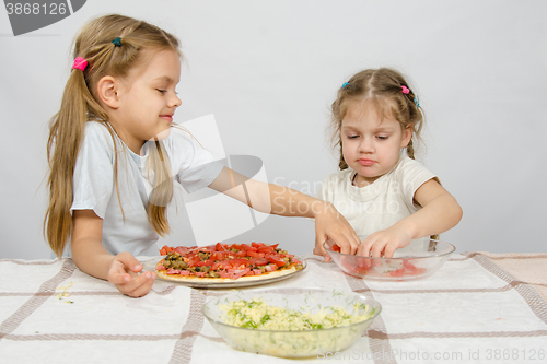 Image of Two little girls at the table spread on tomato pizza