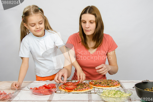 Image of  Six-year girl helps mother spread on tomato pizza