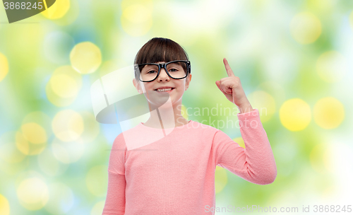 Image of happy little girl in eyeglasses pointing finger up