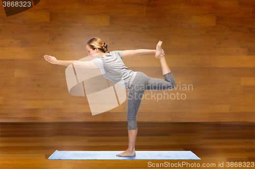 Image of woman making yoga in lord of the dance pose on mat