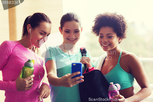 Image of happy women with bottles and smartphone in gym