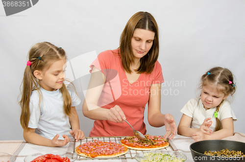 Image of Two little girls sitting at the kitchen table and watch as a mother preparing a pizza