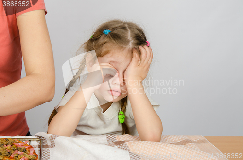 Image of Little girl wearily rubbing his eyes at the kitchen table while Mom cooks