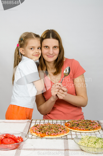 Image of Daughter hugging her mother six years, which is preparing a pizza