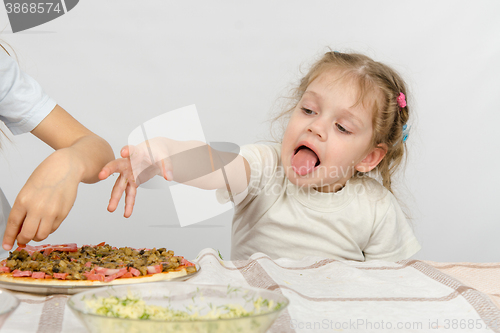 Image of Little girl with tongue sticking out a hand to pull the pizza, which prepares her older sister