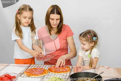 Image of The eldest daughter helps her mother cook a pizza, and the youngest is watching them