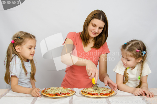 Image of Mom cuts the pizza, and the two little girls eagerly look