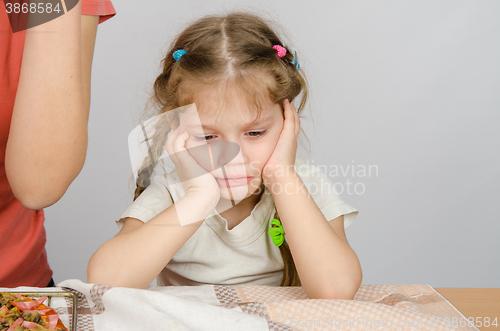 Image of The baby girl with a sad expression on her face sitting at the kitchen table