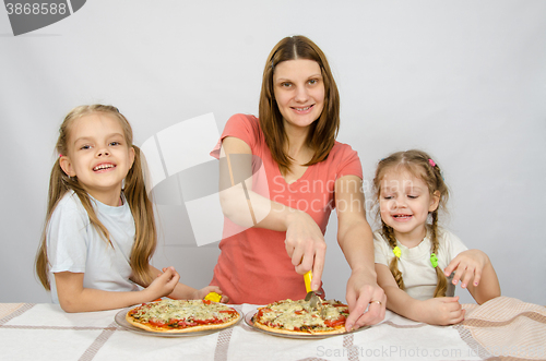 Image of Mother and two little daughters happy sitting at a table with two pizzas