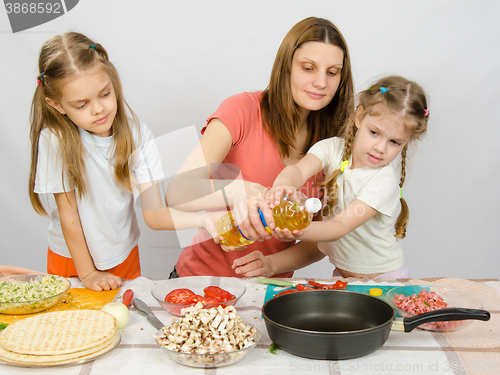 Image of Two little girls at the kitchen table with enthusiasm to help my mother to pour vegetable oil in a frying pan