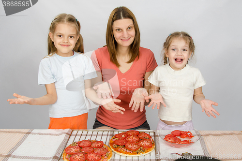 Image of Mom with two young daughters happily show made pizza with tomatoes