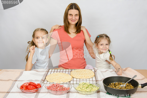 Image of Mother with two daughters at the kitchen table are going to cook a pizza and a fun look into the frame