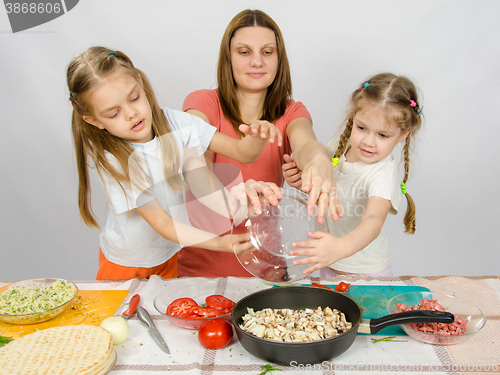Image of Mother with two daughters at the kitchen table with a plate of mushrooms is poured into the pan
