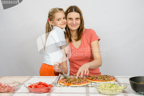 Image of Daughter hugging her mother, which makes pizza at the table