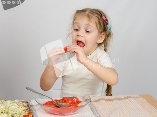 Image of A little girl tries to stick to widely open mouth large slice of tomato