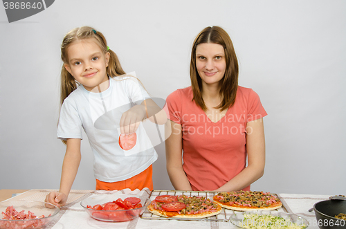 Image of Six-year girl puts on the pizza tomatoes under the supervision of mum