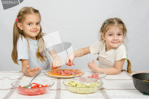 Image of Two little happy girl at the table spread on the pizza ingredients