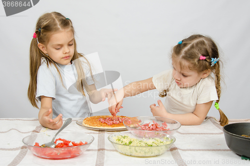 Image of Six-year girl observes and controls her younger sister puts on the pizza ingredients