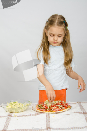 Image of Little six year old girl standing at the table and sprinkle with grated cheese pizza