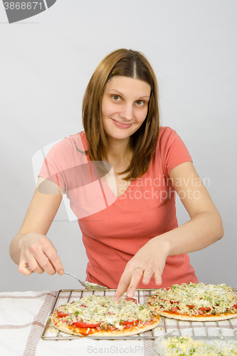 Image of The girl at the table puts toppings on a pizza with a satisfied look on his face