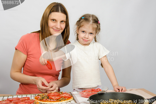 Image of Little five-year girl helps mother spread on the pizza ingredients