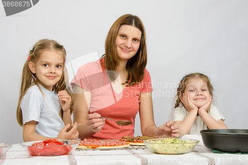 Image of Mum with two little girls sitting at the kitchen table preparing a pizza