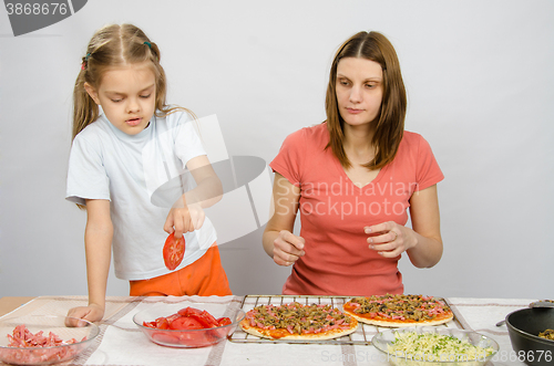 Image of Six year old girl takes a plate of cutting tomatoes for pizza under the supervision of mum