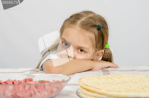 Image of Little girl sitting at a table with his head on his hand with a smile and looking at the food in front of her