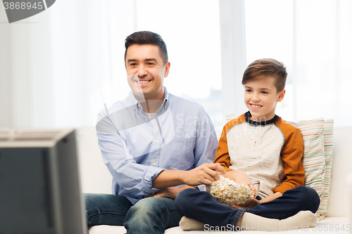Image of smiling father and son watching tv at home