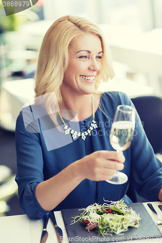 Image of happy woman drinking champagne at restaurant