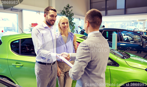 Image of happy couple with car dealer in auto show or salon