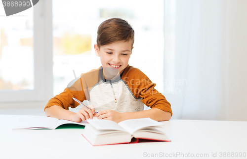 Image of smiling student boy writing to notebook at home