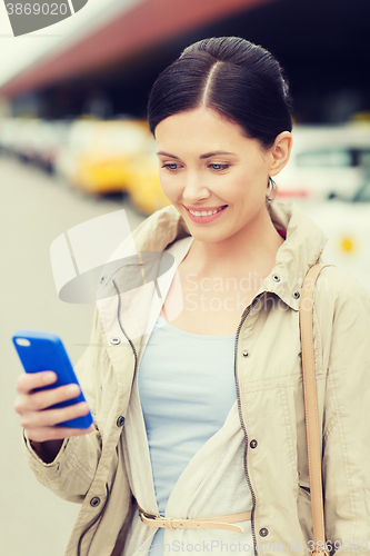 Image of smiling woman with smartphone over taxi in city