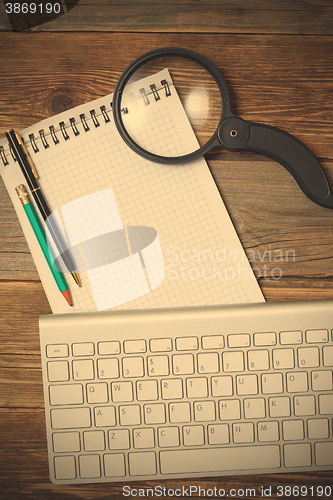 Image of computer keyboard, ballpoint pen, pencil, notepad and magnifying