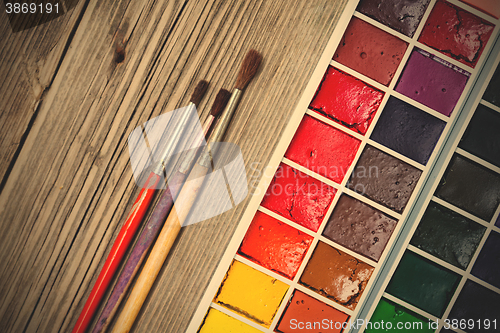 Image of paint-box and three brushes on a textured surface