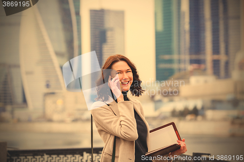 Image of smiling middle-aged woman with notebook talking on the phone