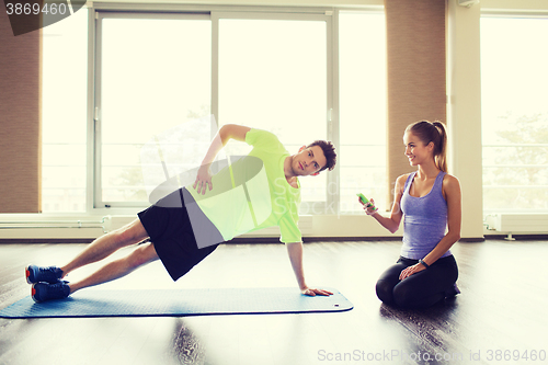 Image of man and woman doing plank exercise on mat in gym