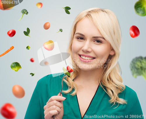 Image of smiling young woman eating vegetable salad