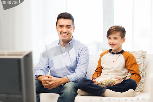 Image of smiling father and son watching tv at home