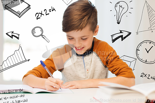 Image of smiling student boy writing to notebook at home