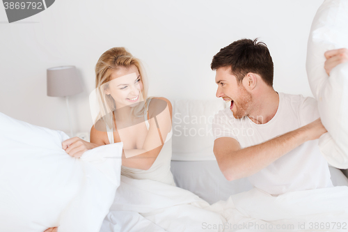 Image of happy couple having pillow fight in bed at home