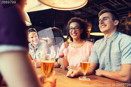 Image of happy friends drinking beer and talking at bar