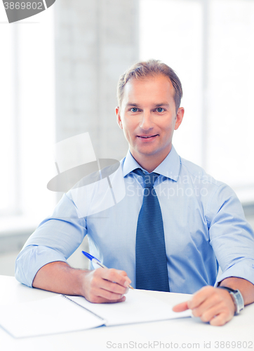 Image of handsome businessman writing in notebook