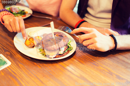Image of close up of friends hands sharing burger at bar
