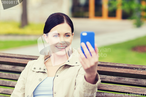 Image of smiling woman taking picture with smartphone