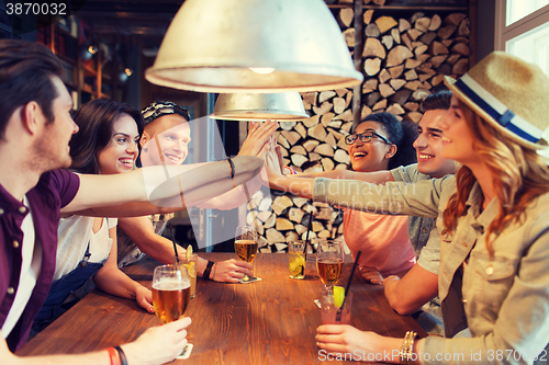 Image of happy friends with drinks making high five at bar